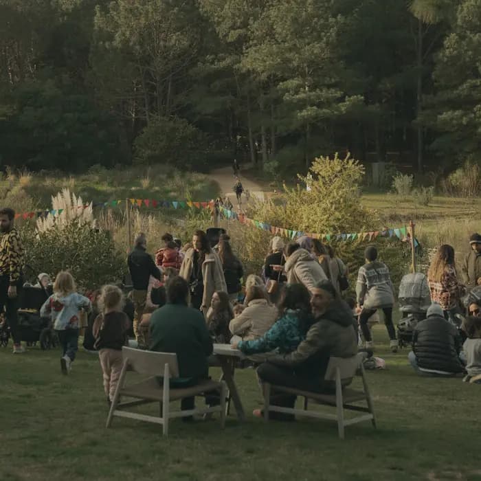 Evento al aire libre con familias disfrutando en un parque, rodeados de naturaleza y decoración con banderines coloridos.